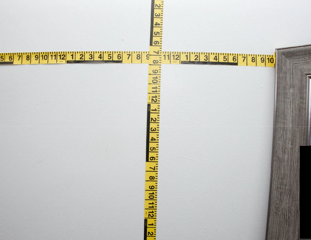 Intersecting yellow measuring tapes across a pale wall.