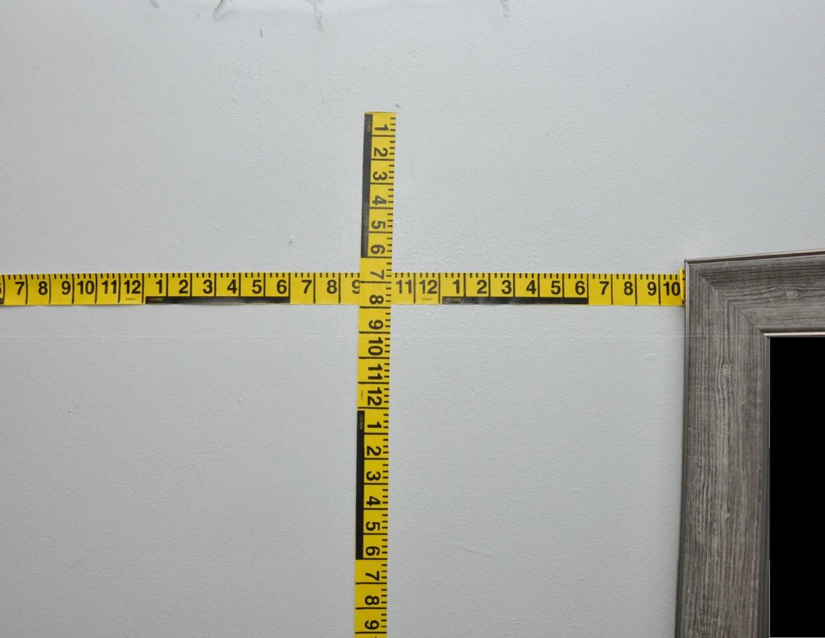 Intersecting yellow measuring tapes across a pale wall.