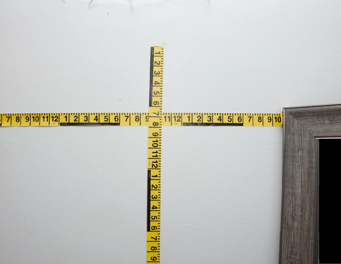 Intersecting yellow measuring tapes across a pale wall.