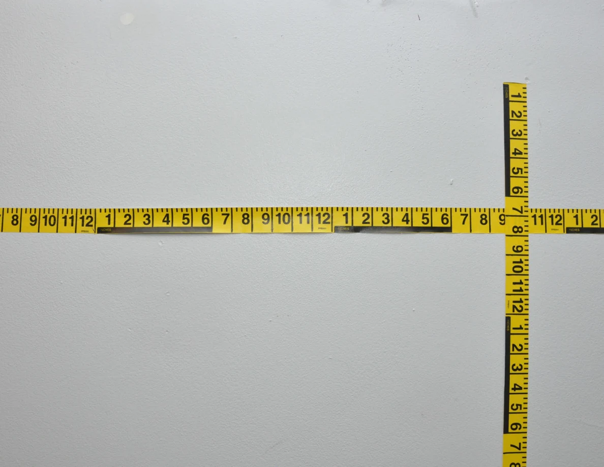Intersecting yellow measuring tapes across a pale wall.