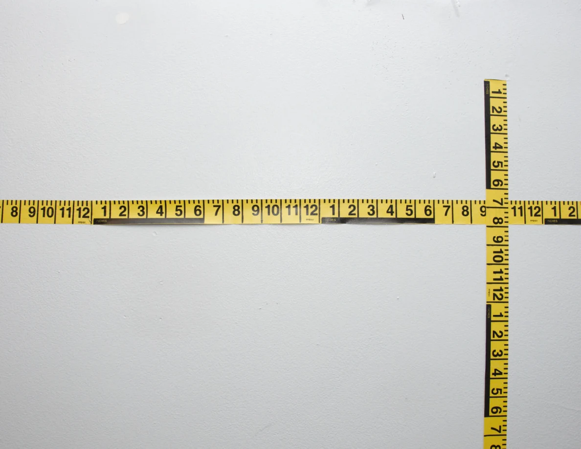 Intersecting yellow measuring tapes across a pale wall.