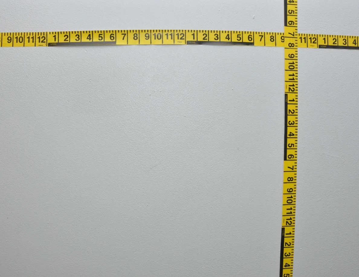 Intersecting yellow measuring tapes across a pale wall.
