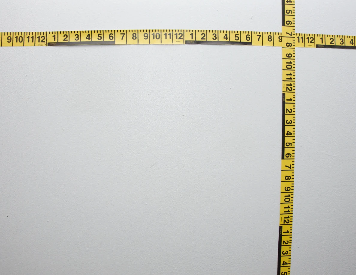 Intersecting yellow measuring tapes across a pale wall.
