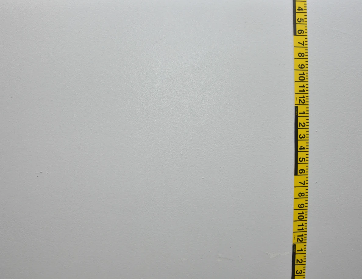 Vertical yellow measuring tape on a pale wall.