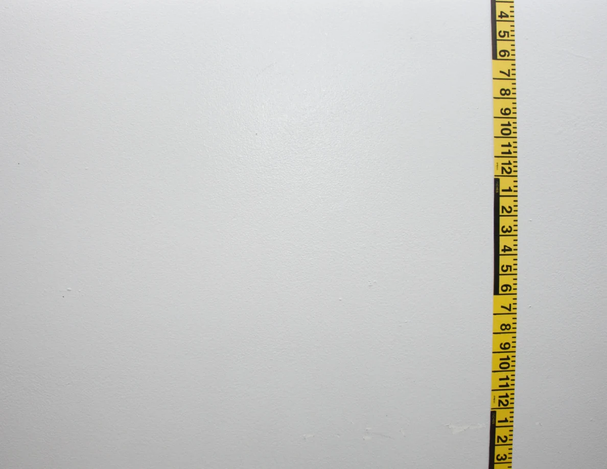 Vertical yellow measuring tape on a pale wall.