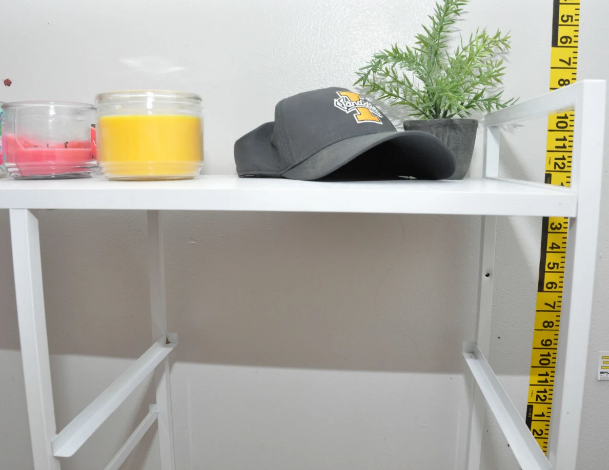 Candles, a dark cap and small plant on a white cabinet beside measuring tape.