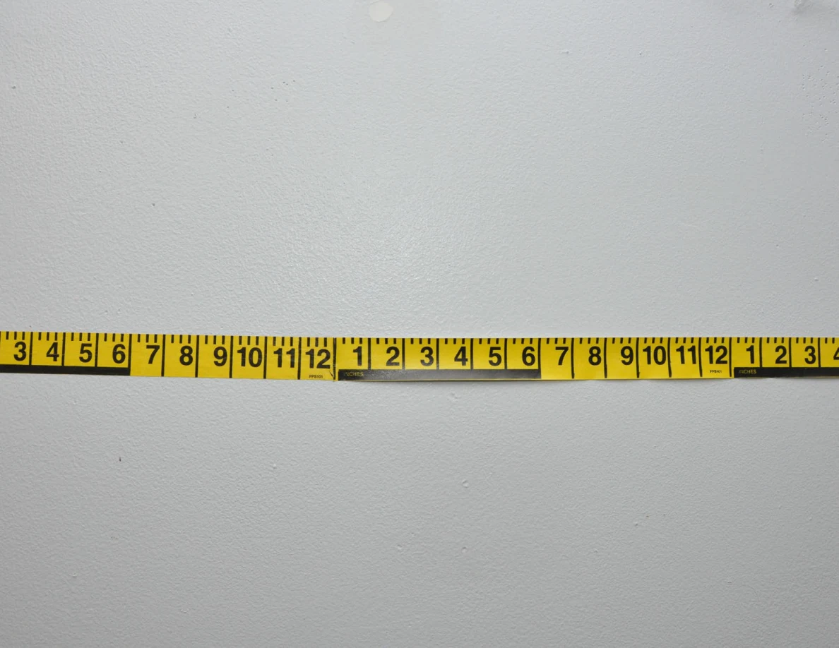 Horizontal yellow measuring tape across a pale wall.