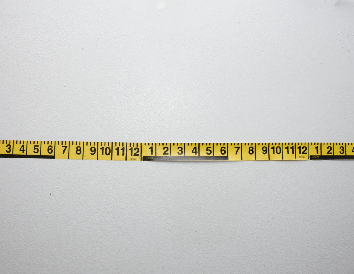 Horizontal yellow measuring tape across a pale wall.