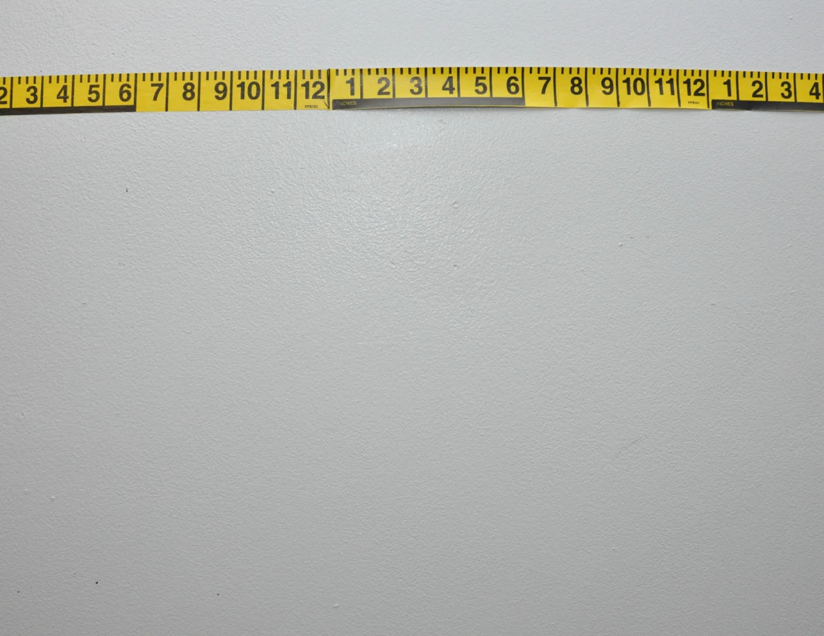 Horizontal yellow measuring tape across a pale wall.