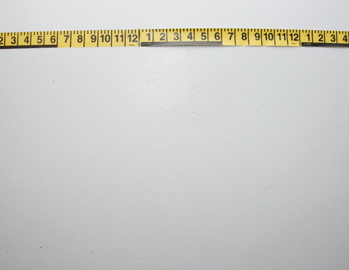 Horizontal yellow measuring tape across a pale wall.