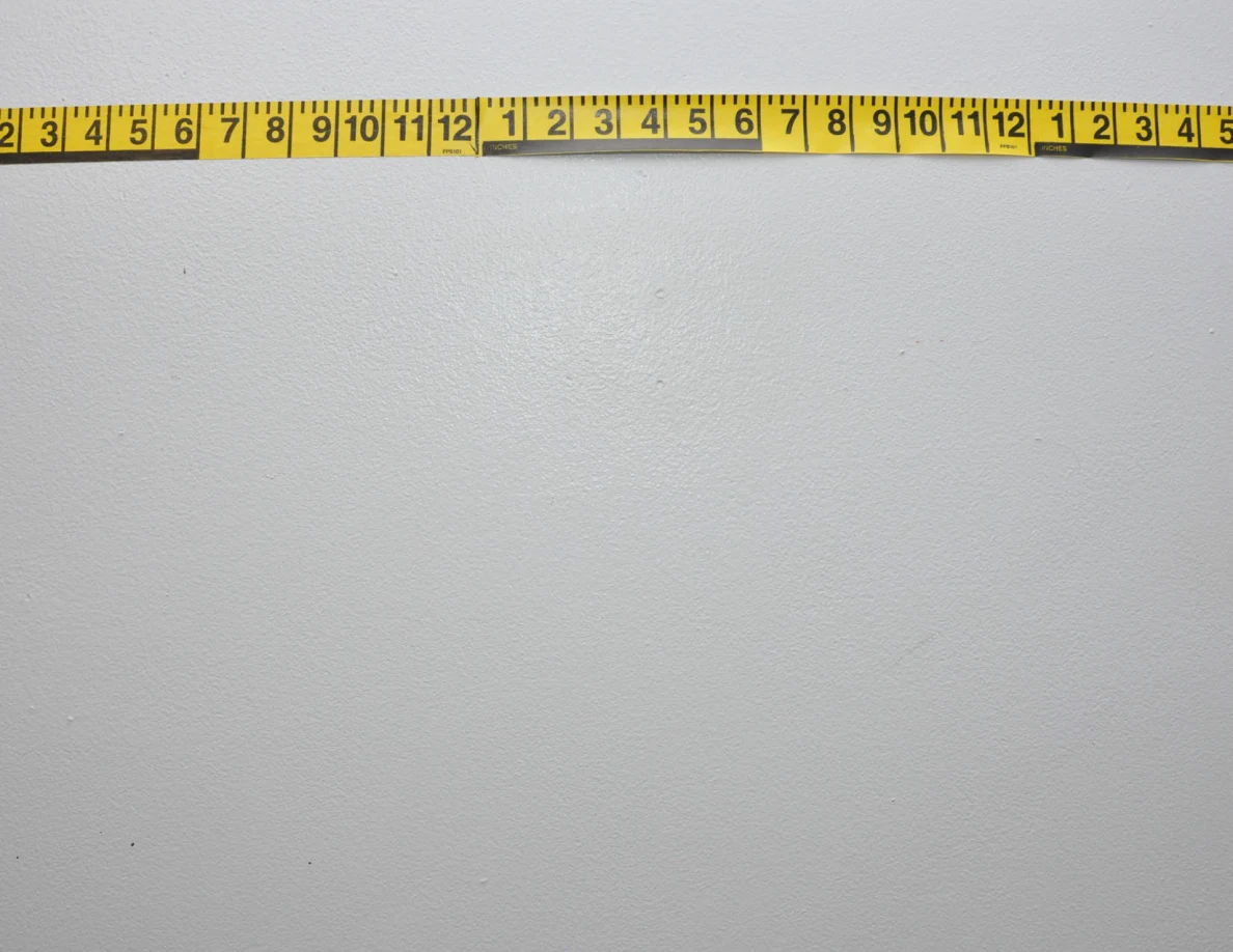 Horizontal yellow measuring tape across a pale wall.
