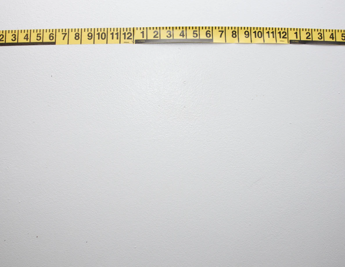 Horizontal yellow measuring tape across a pale wall.