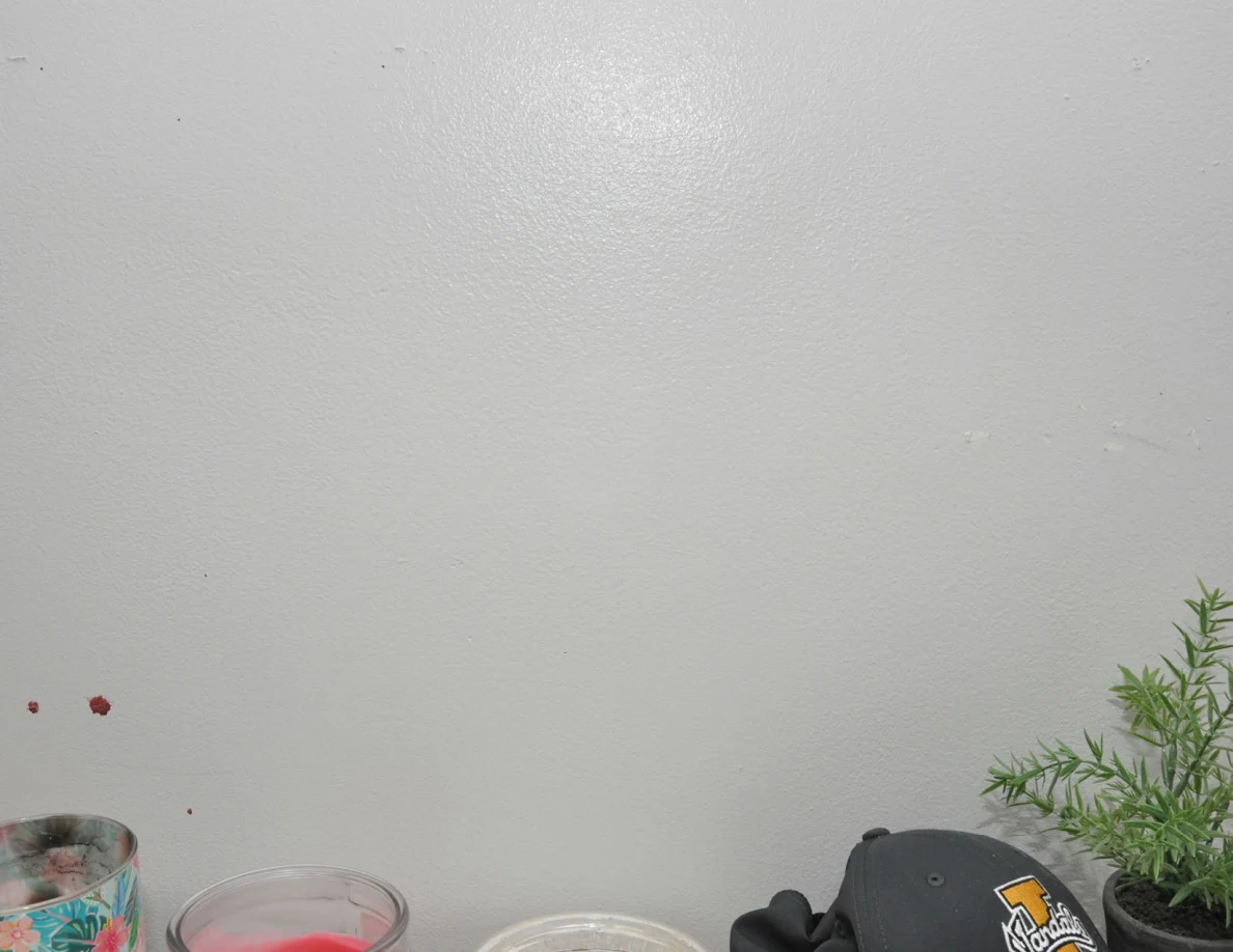 Pale wall above candles, a cap and small plant.