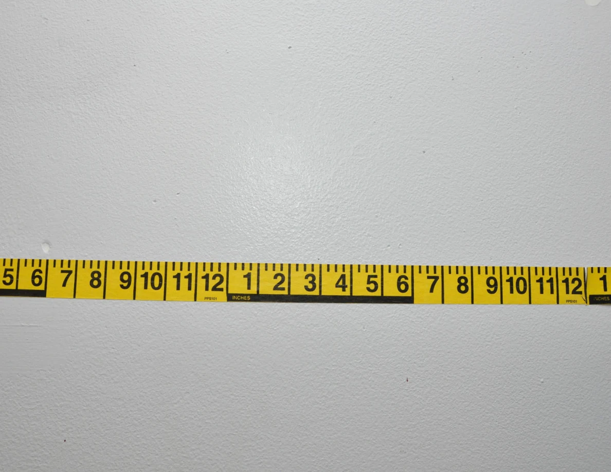 Horizontal yellow measuring tape across a pale wall.