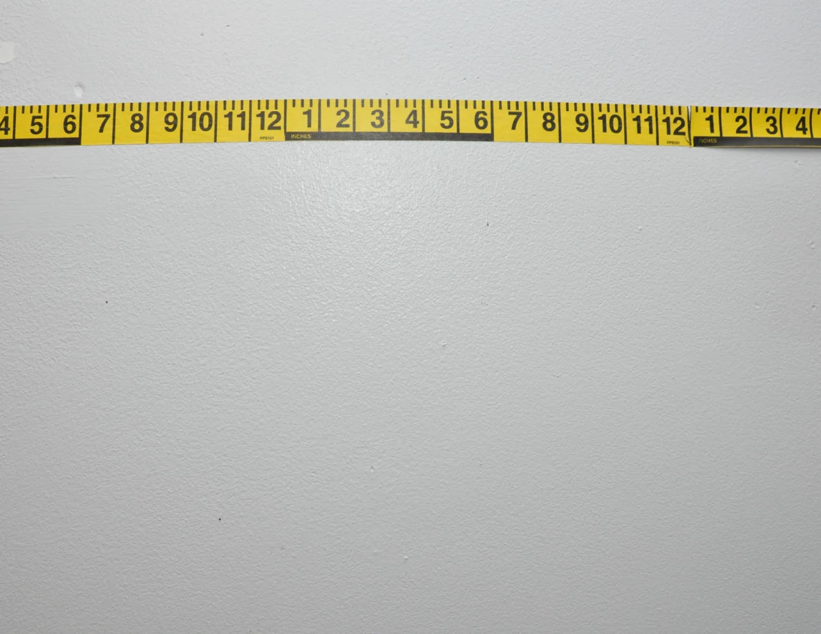 Horizontal yellow measuring tape across a pale wall.