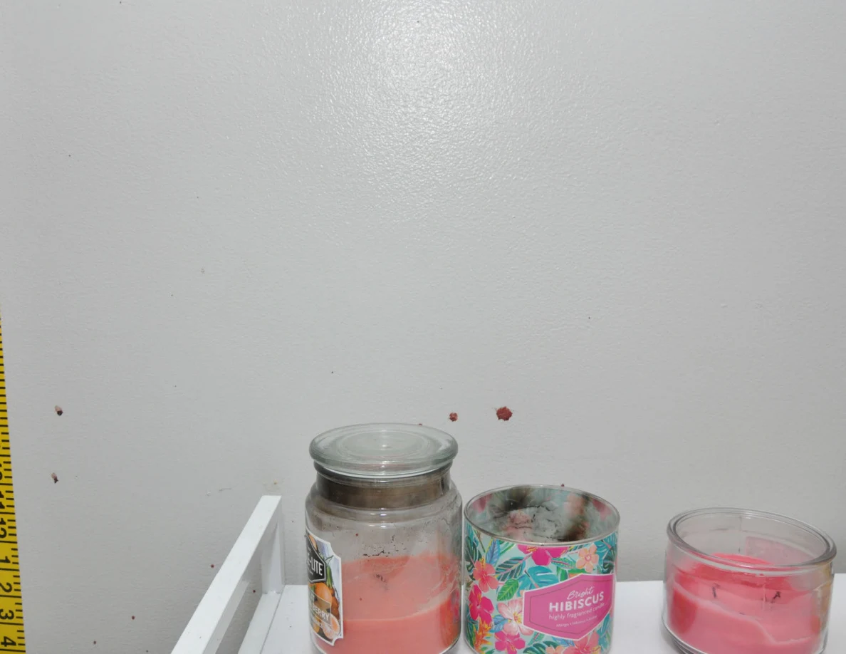 Candles on a white cabinet below reddish wall spots.