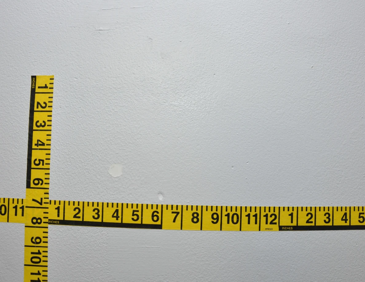 Intersecting yellow measuring tapes across a pale wall.