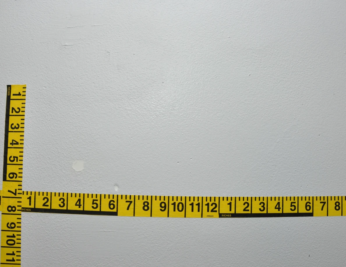 Intersecting yellow measuring tapes across a pale wall.