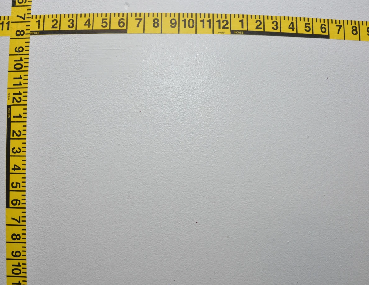 Intersecting yellow measuring tapes across a pale wall.