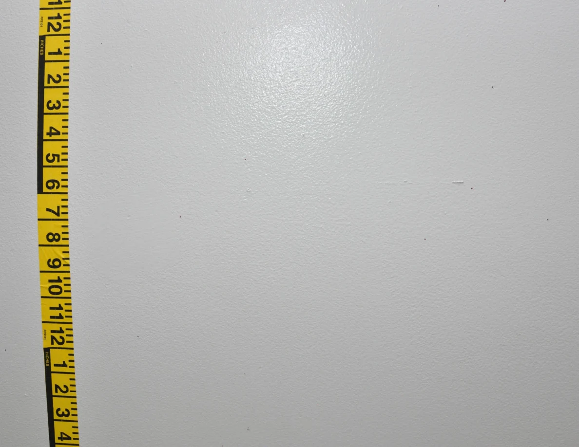 Vertical yellow measuring tape beside small wall marks.