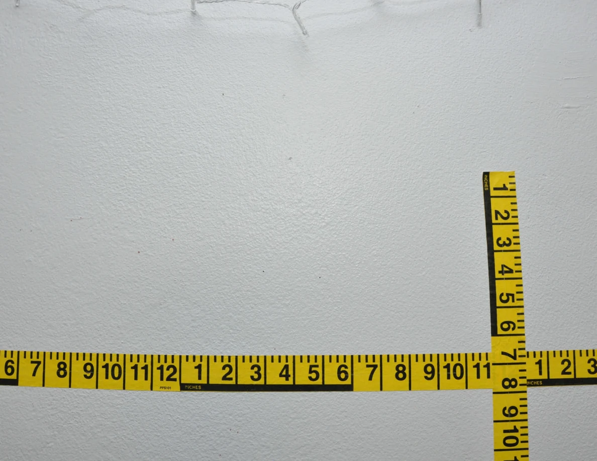 Intersecting yellow measuring tapes on a wall.