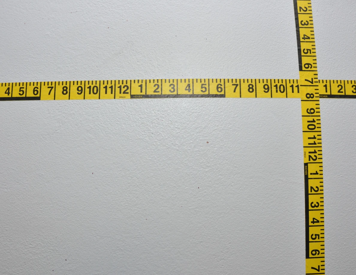 Intersecting yellow measuring tapes on a wall.