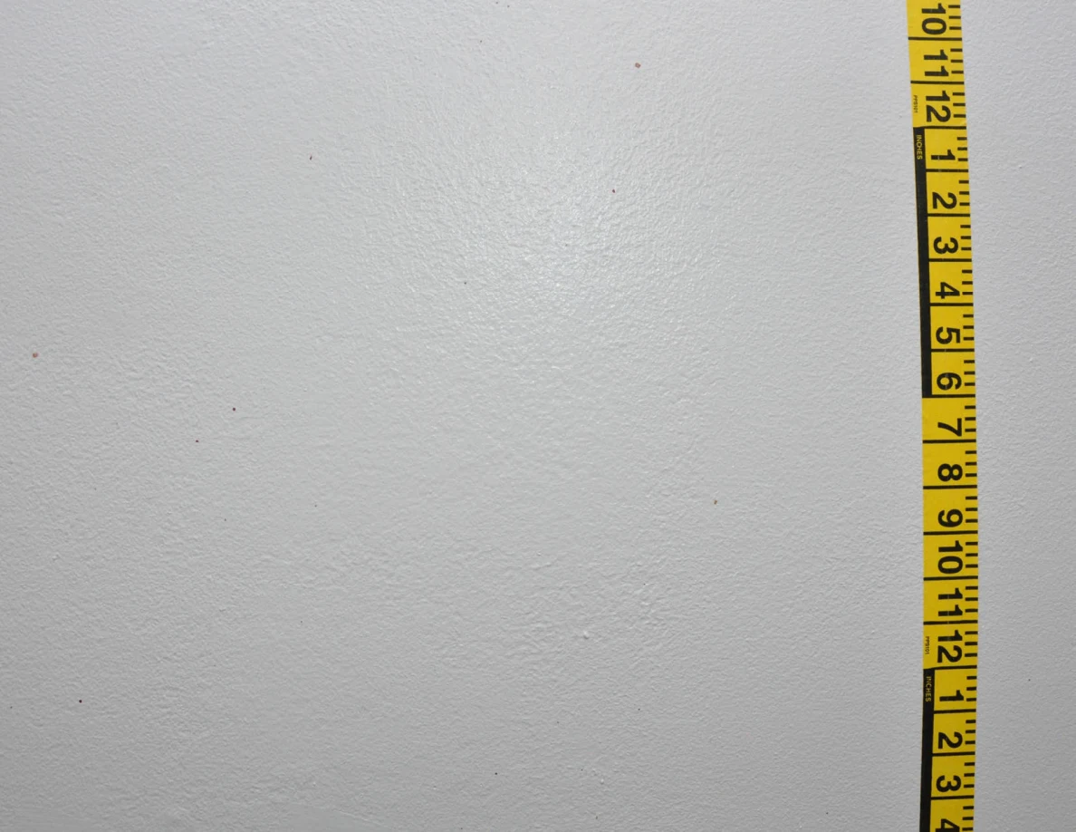 Vertical yellow measuring tape beside sparse wall marks.