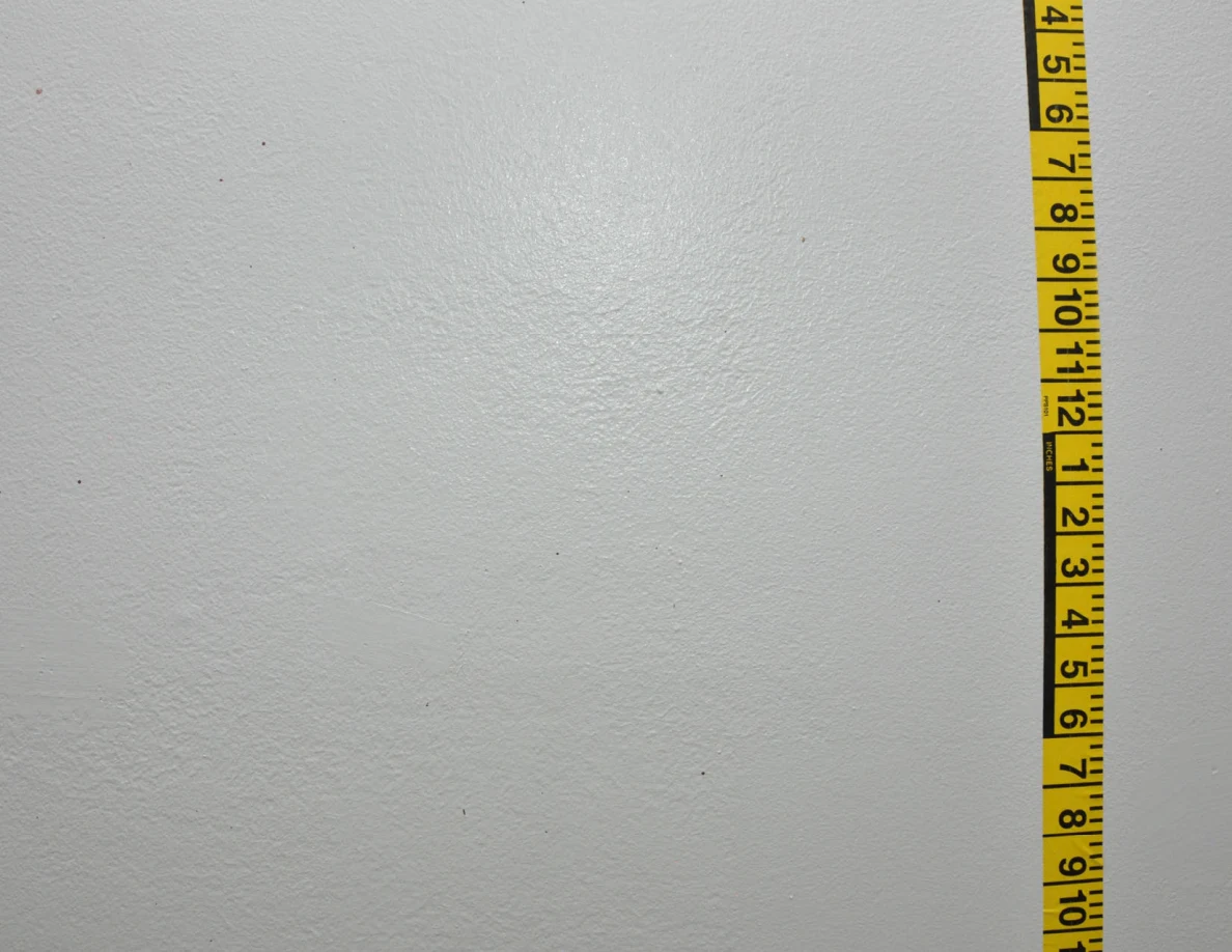 Vertical yellow measuring tape beside sparse wall marks.