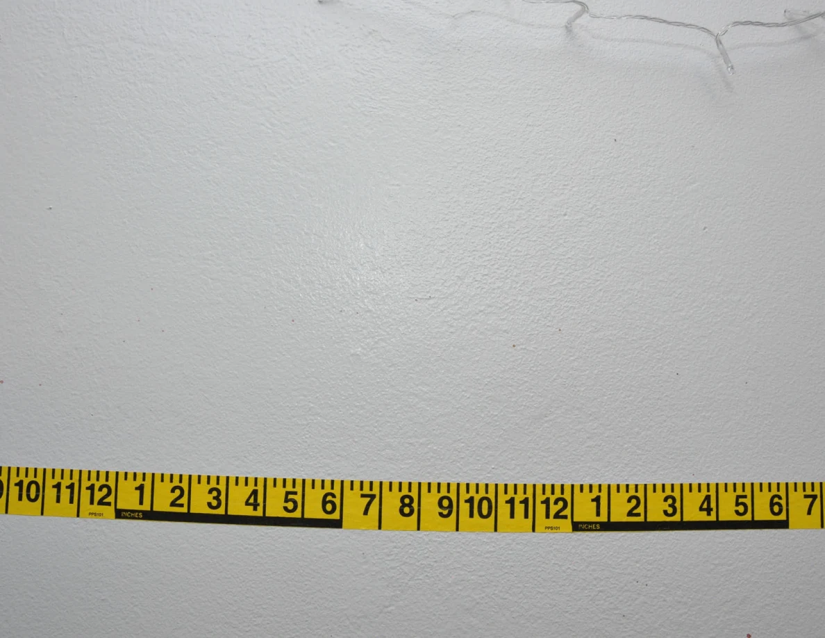 Horizontal yellow measuring tape across a pale wall.
