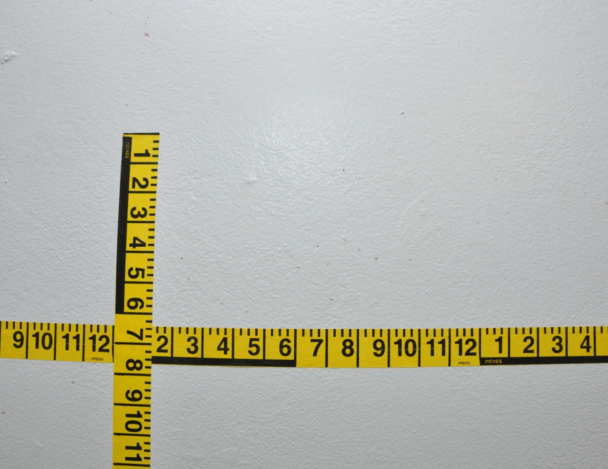 Intersecting yellow measuring tapes on a pale wall.