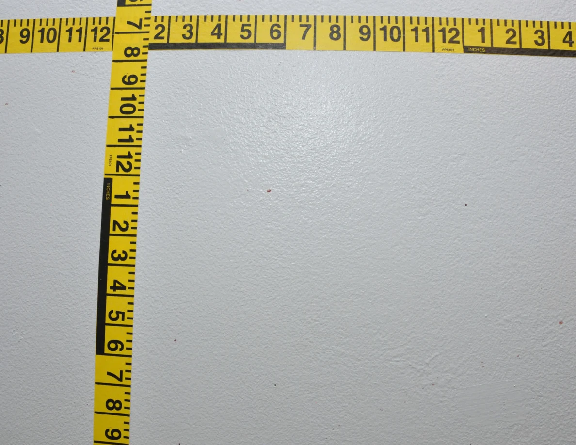 Intersecting yellow measuring tapes beside small reddish wall spots.