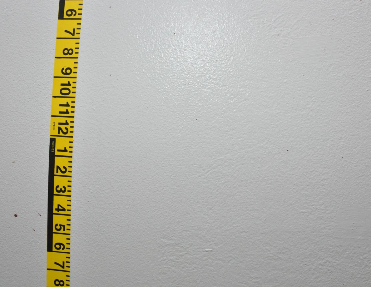 Vertical yellow measuring tape beside small reddish wall spots.