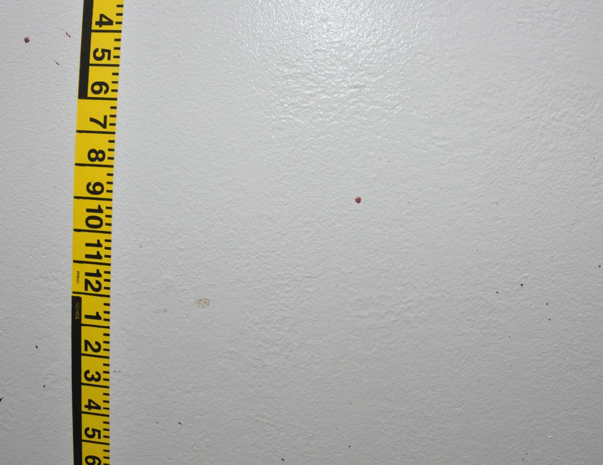 Vertical yellow measuring tape beside small reddish wall spots.
