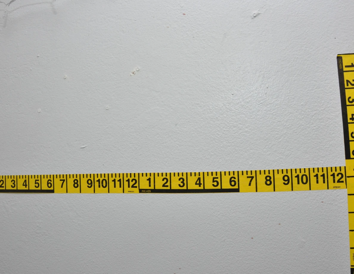 Intersecting yellow measuring tapes across a pale wall.