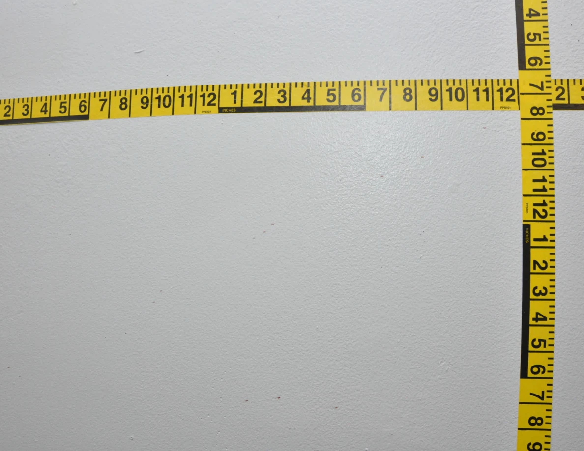 Intersecting yellow measuring tapes across a pale wall.