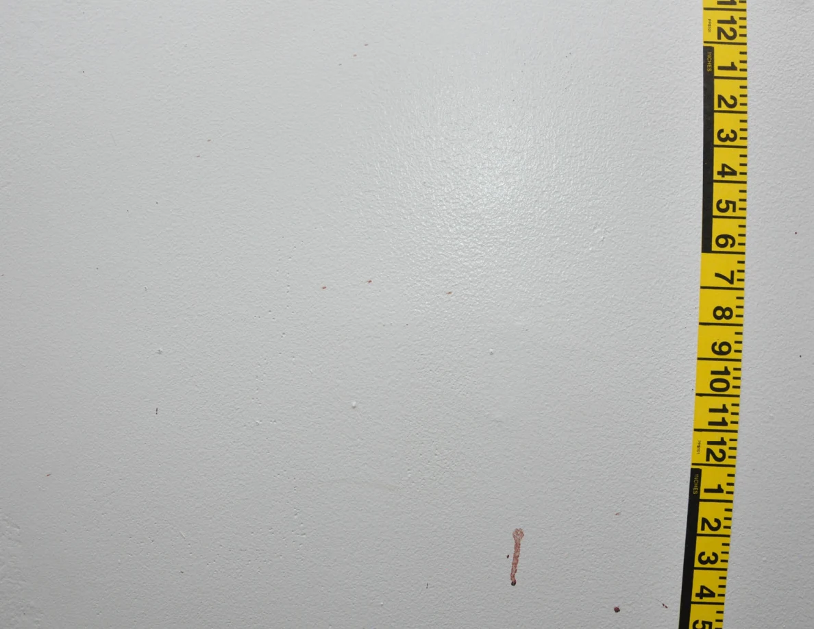 Vertical yellow measuring tape beside reddish wall spots and short streaks.