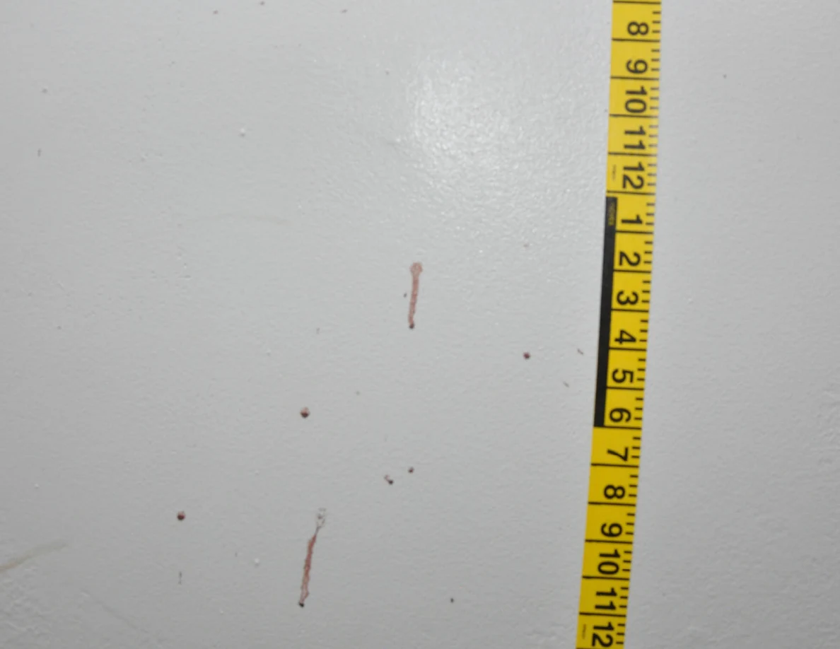 Vertical yellow measuring tape beside reddish wall spots and short streaks.