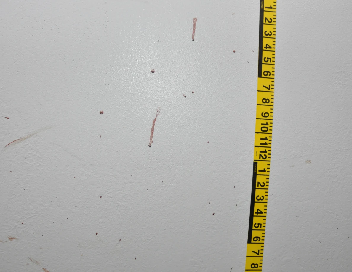 Vertical yellow measuring tape beside reddish wall spots and short streaks.