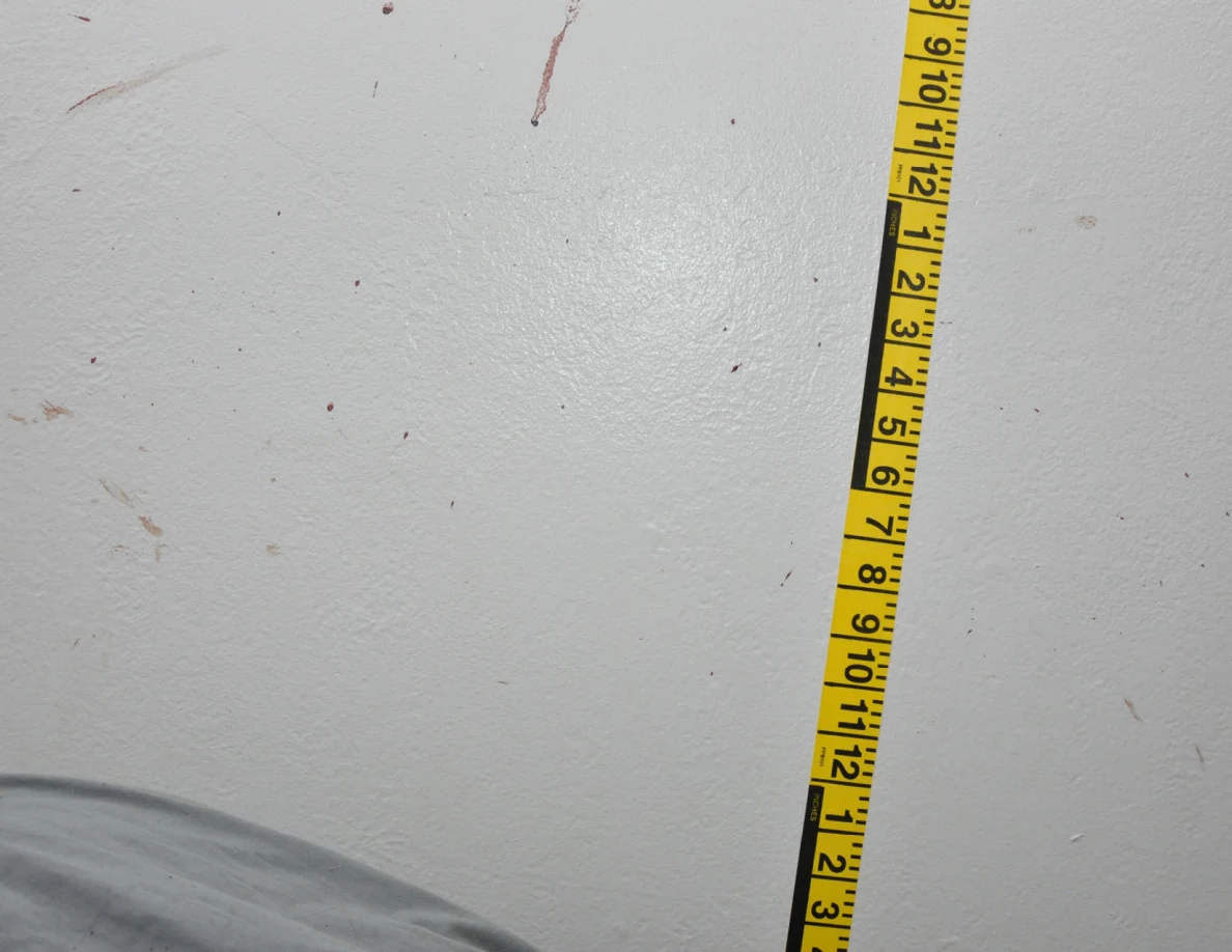 Vertical yellow measuring tape beside reddish wall spots and short streaks.
