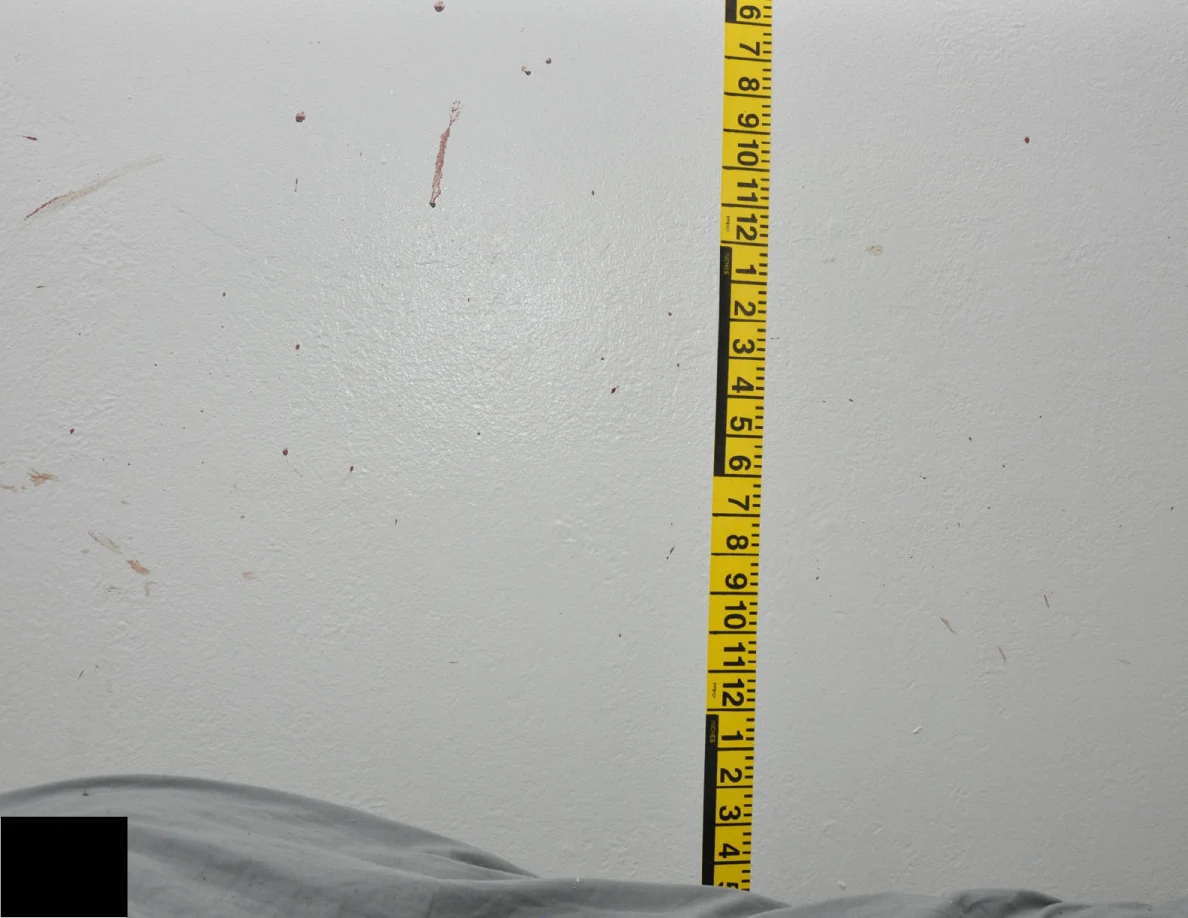 Vertical yellow measuring tape beside reddish wall spots and short streaks.