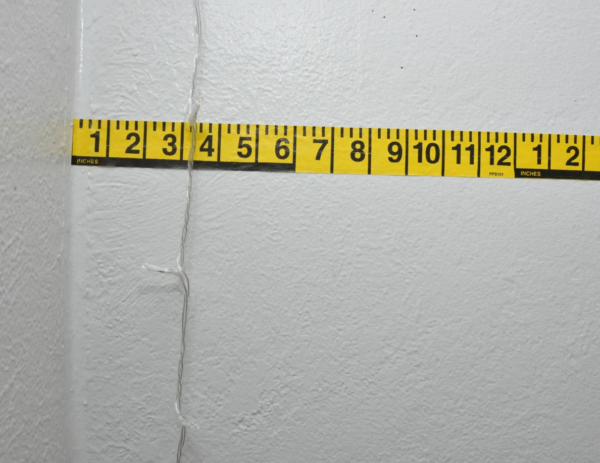 String-light cable against a pale wall beside yellow measuring tape.