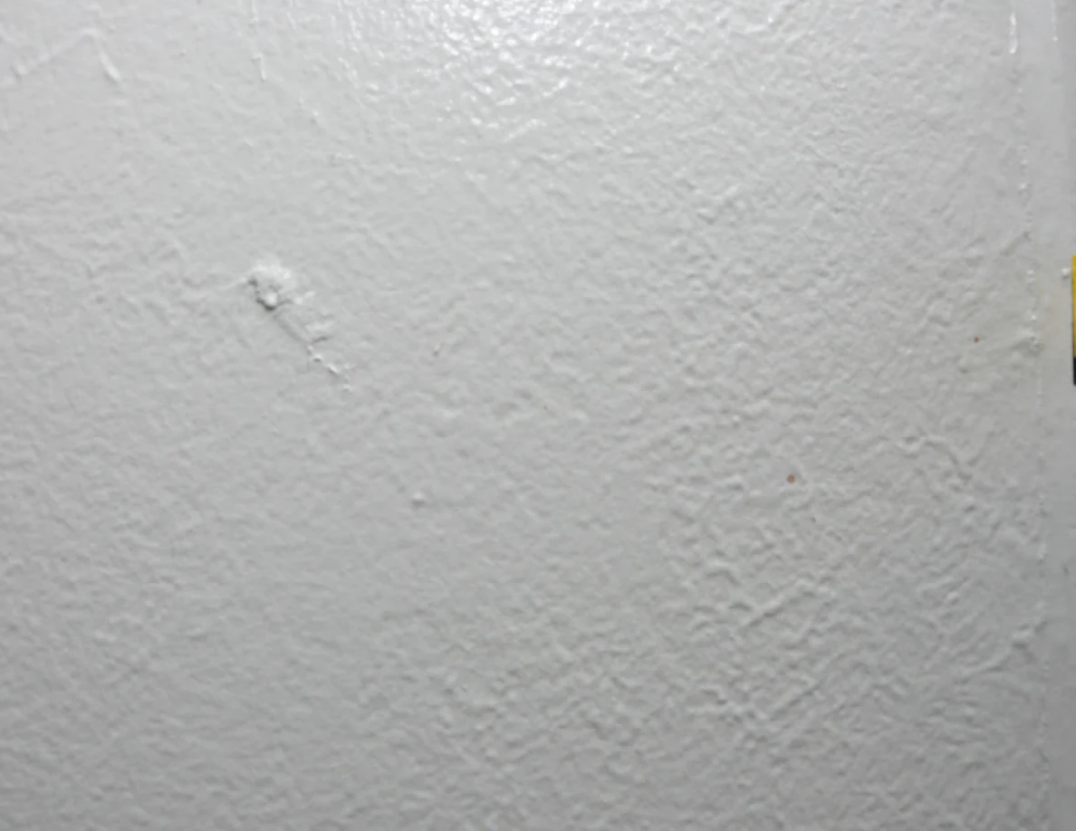 Close view of small marks on a pale textured wall.