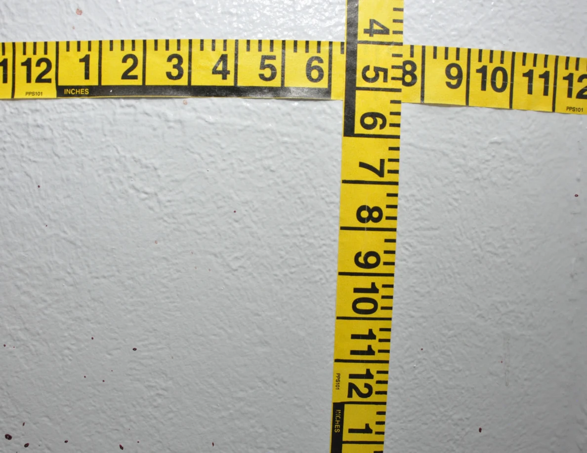 Intersecting yellow measuring tapes beside reddish wall spots.