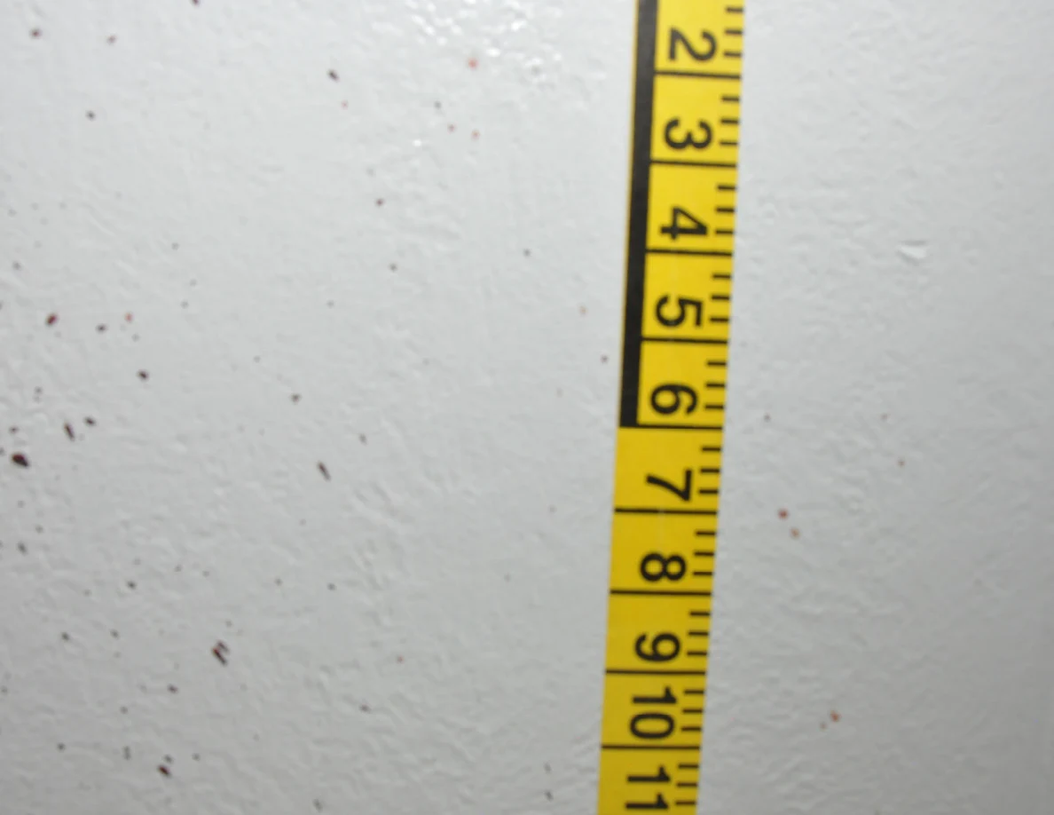 Vertical yellow measuring tape beside reddish wall spots.