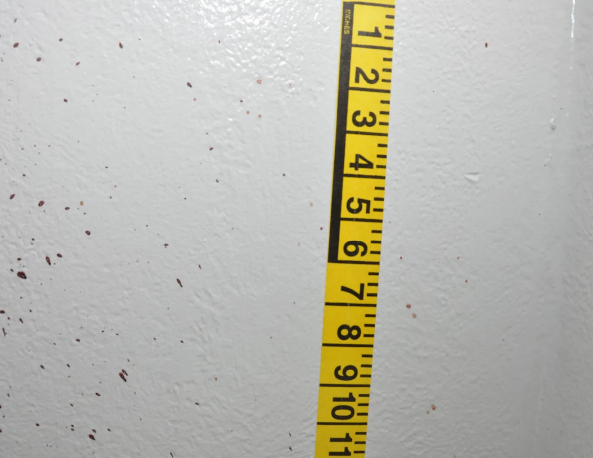 Vertical yellow measuring tape beside reddish wall spots.