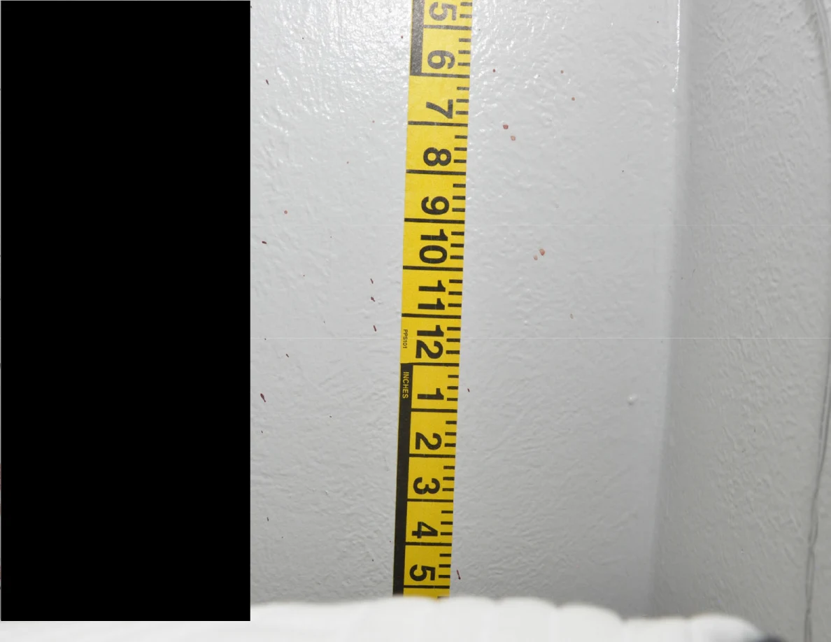 Vertical yellow measuring tape on a wall beside a black redaction.