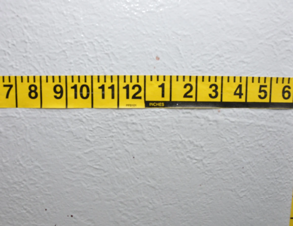 Horizontal yellow measuring tape beside small wall specks.