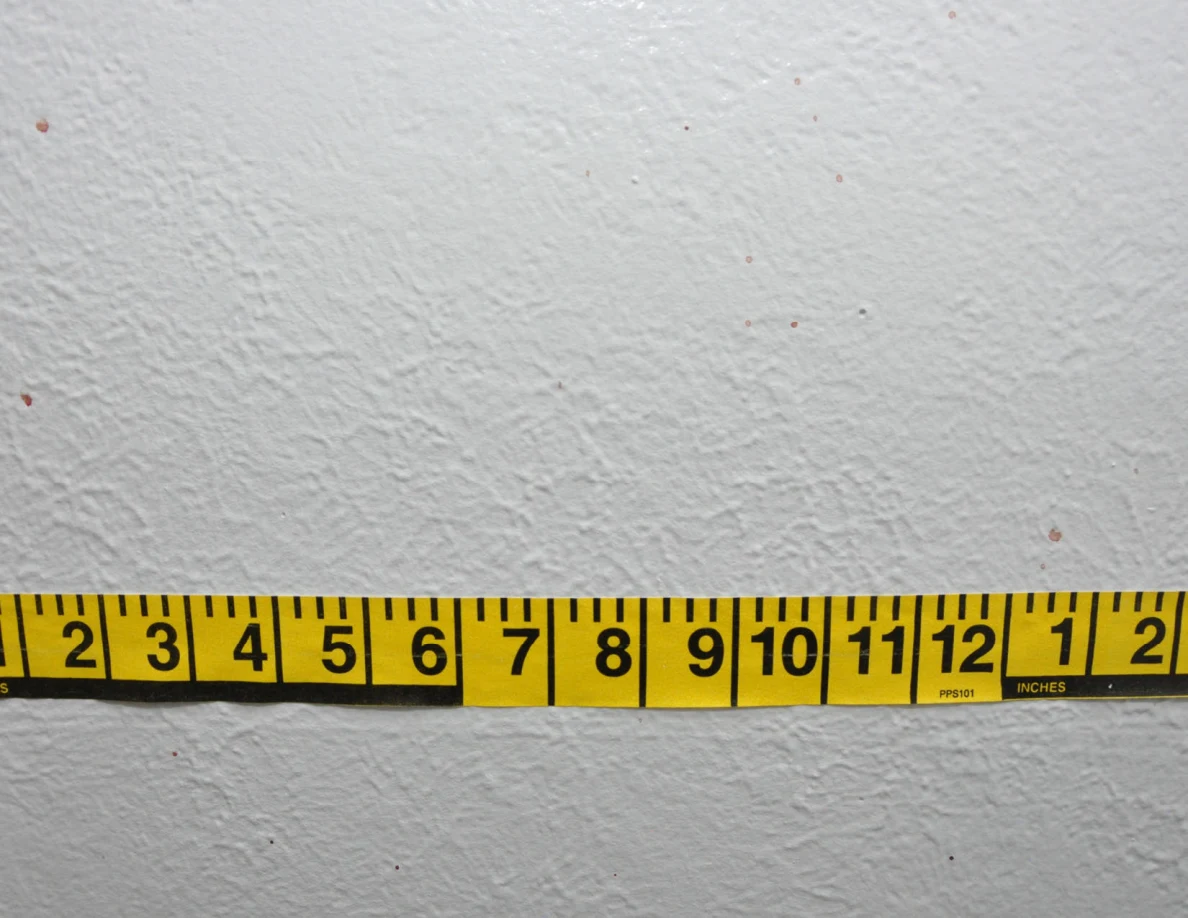 Horizontal yellow measuring tape beside small wall spots.