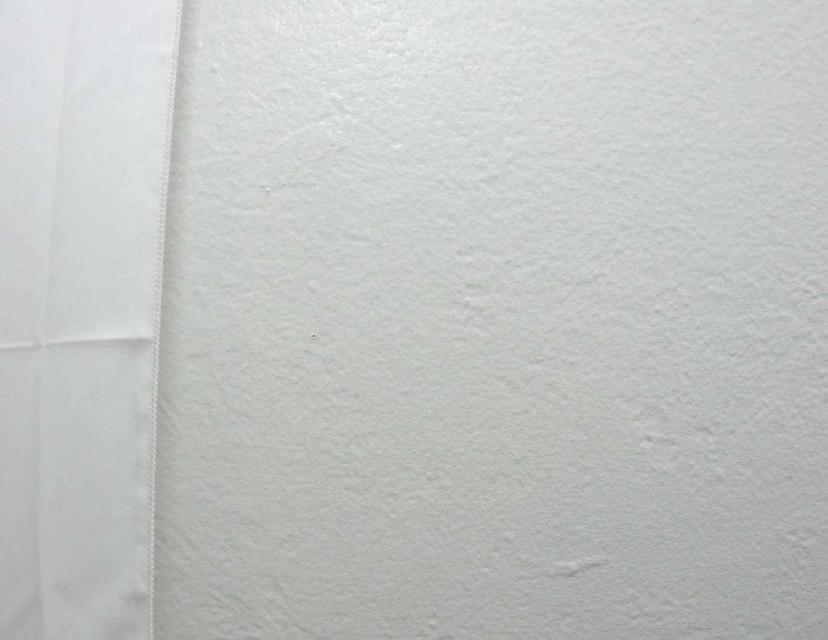 Edge of a white fabric wall hanging against a pale wall.