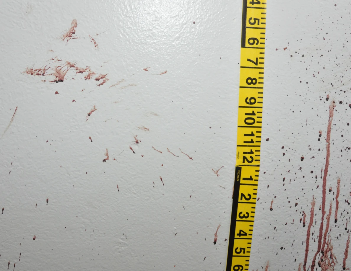 Reddish wall smears and streaks beside vertical yellow measuring tape.